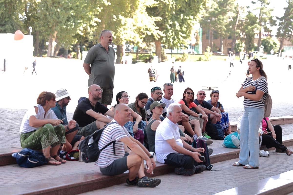 Guide briefing for the group Guide speaking to a seated group during an outdoor visit in Uzbekistan