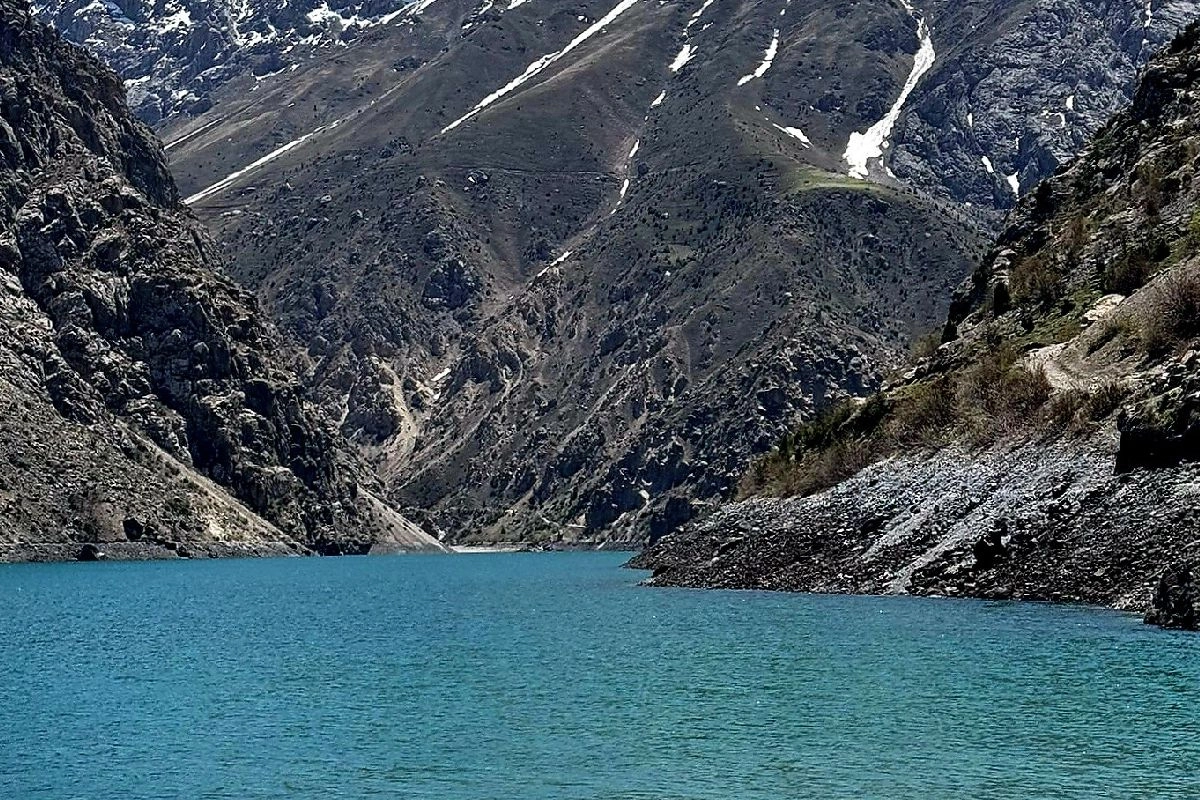 Lac Hazorchashma turquoise au pied de versants striés de neige
