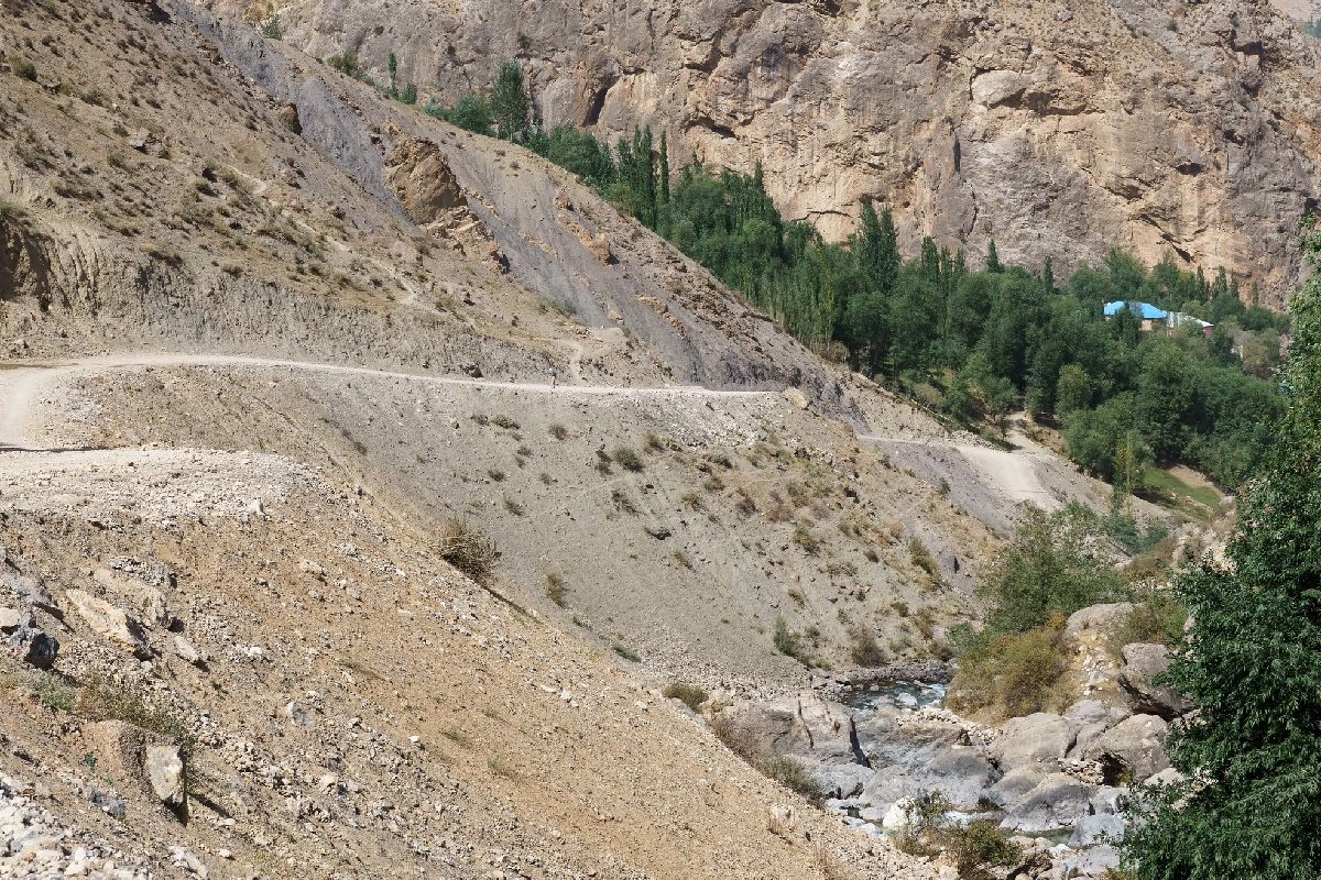 Piste de montagne non goudronnée au-dessus d’un lit de rivière rocheux dans la vallée de Ching