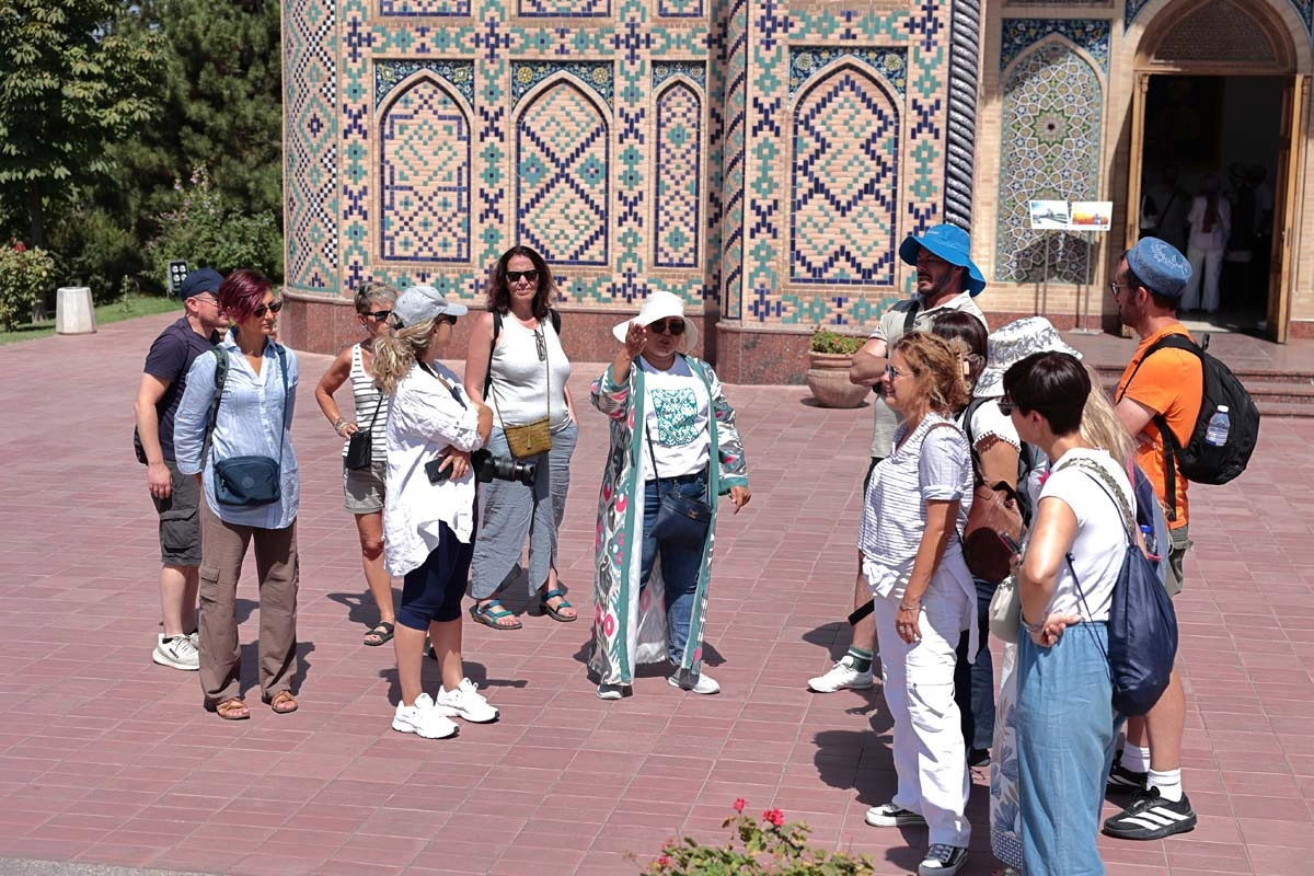 Small travel group listening to a guide beside a tiled historic facade in Uzbekistan