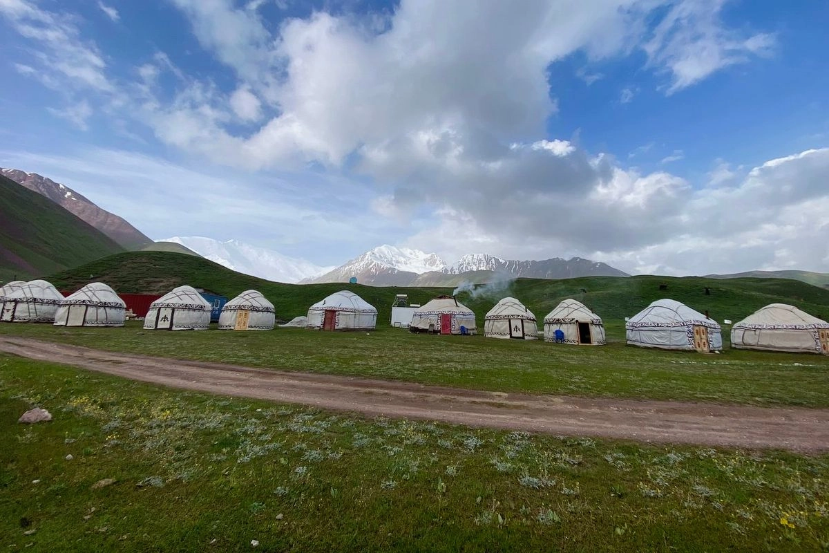 Jurten auf einem grünen Hang vor einer Bergkette — Tulpar CBT Yurt Camp