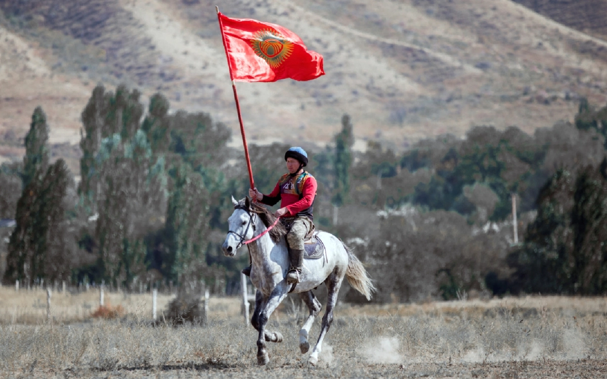 Kyrgyz horseman carrying the national flag in a mountain valley