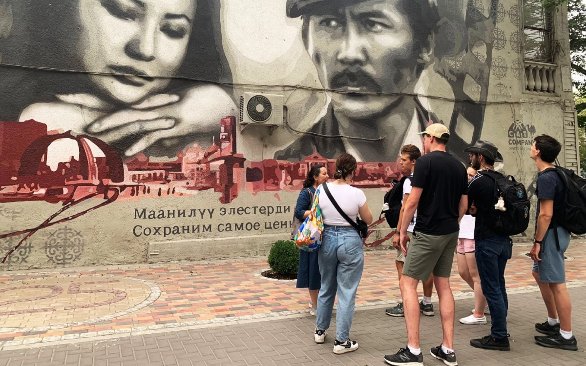Local guide and travelers viewing a Soviet-era mosaic in Bishkek