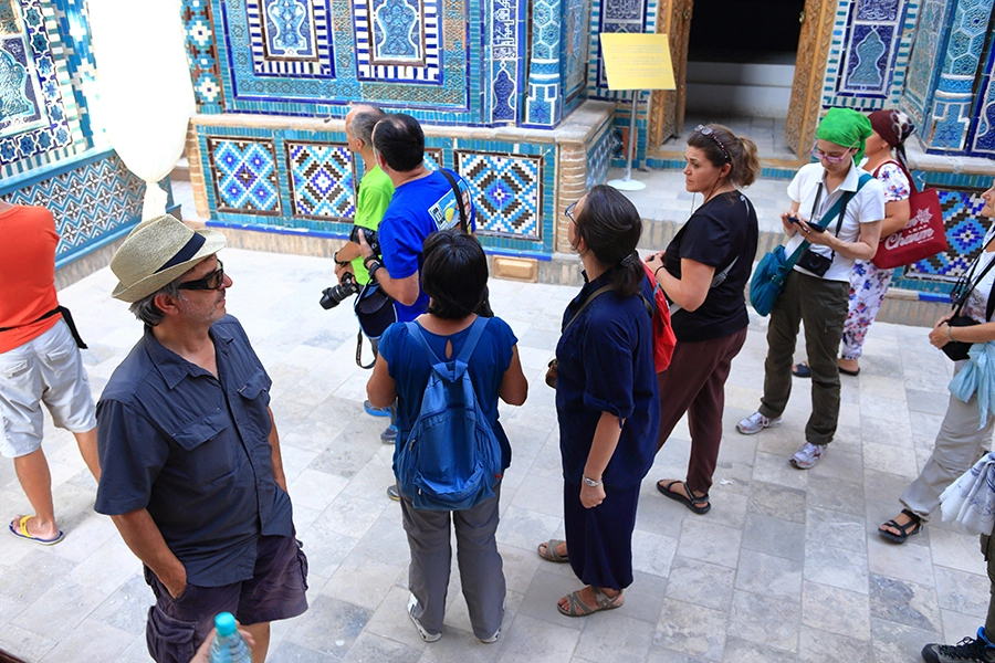 Small tour group listening to the guide near the stunning blue tilework of Shahi-Zinda complex, Samarkand