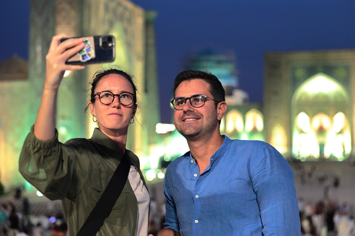 Couple taking a night selfie at the illuminated Registan Square in Samarkand, Uzbekistan