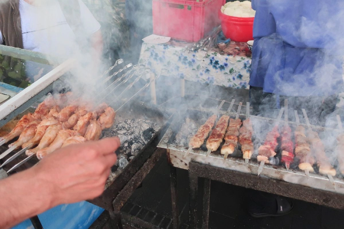 A cook grilling shashlik over charcoal