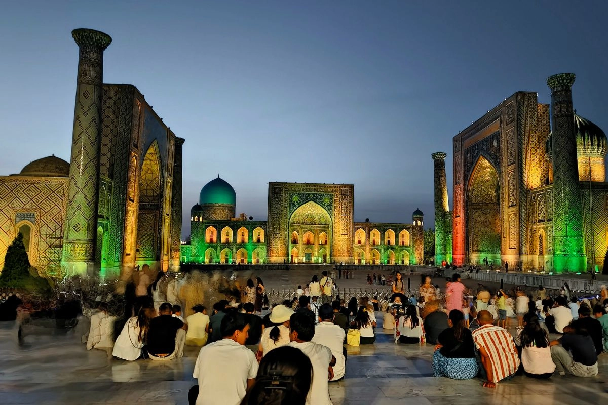 The Registan ensemble in Samarkand illuminated in the evening, with visitors in the square