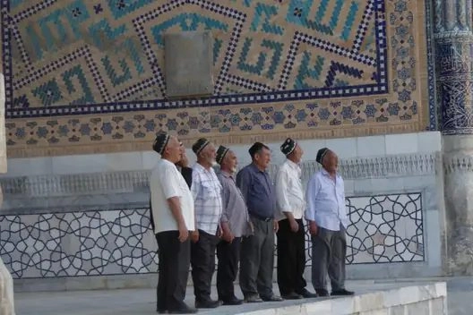 Men in traditional skullcaps beside a wall of blue majolica