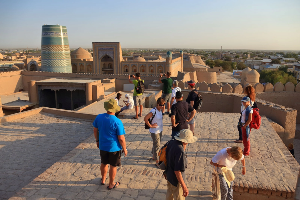 Tourists enjoying sunset views from the fortress walls overlooking Ichan Kala and Kalta Minor in Khiva Uzbekistan