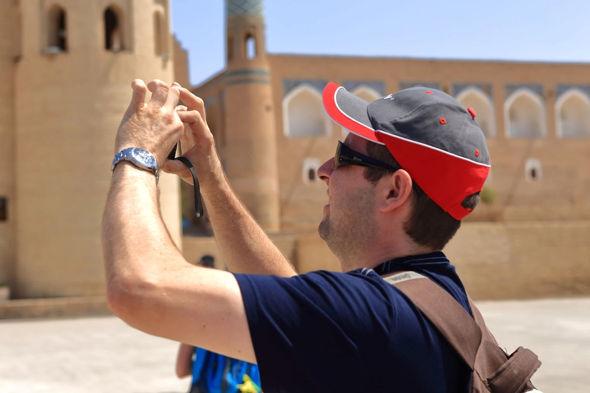 Tourist taking a photo near the minarets and mudbrick walls of Ichan Kala in Khiva Uzbekistan